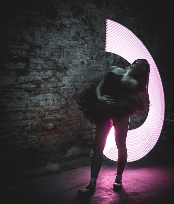 Woman in a graceful yoga pose against a dark granite background with pink light.